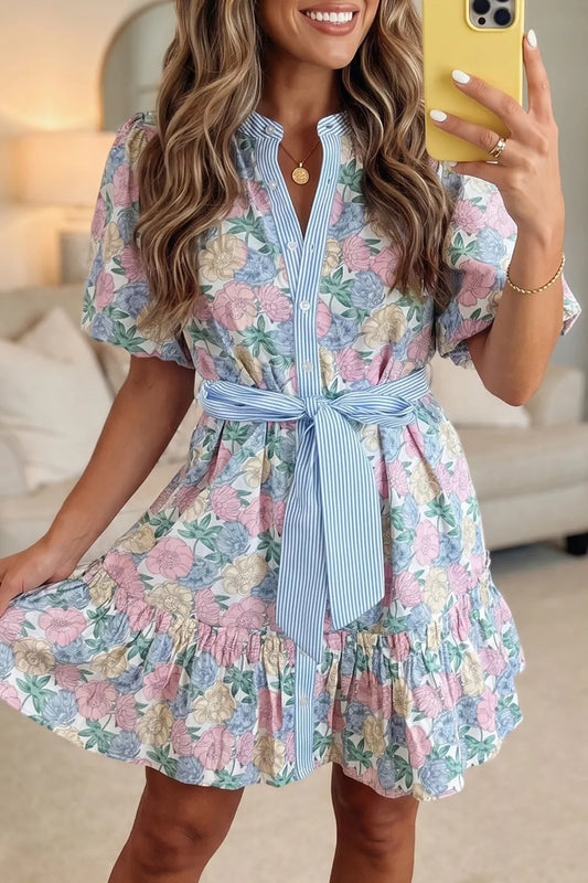 Woman taking a selfie wearing a floral dress with a blue belt in a living room.