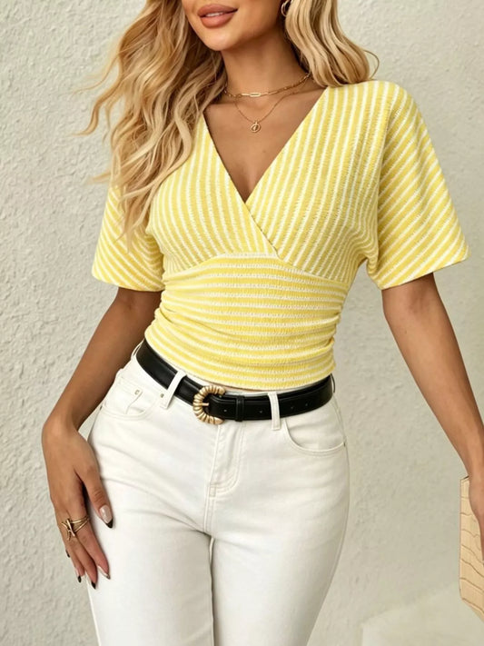 Woman wearing a yellow striped top and white pants against a neutral background